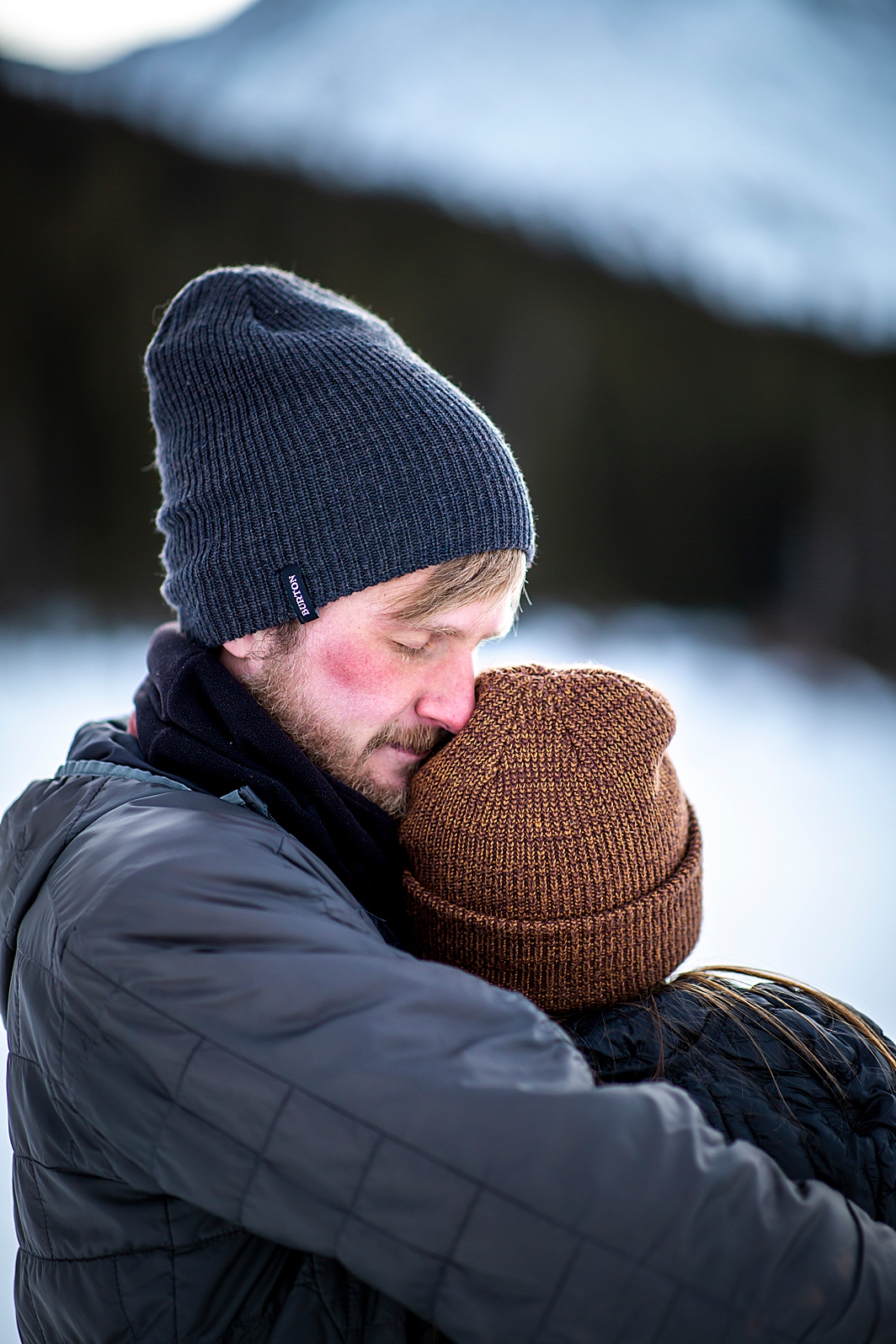 Cute couple photo of man hugging woman in the snow during their winter engagement session in Breckenridge, Colorado taken by Hillary Shedd Photography, Colorado Wedding Photographer.