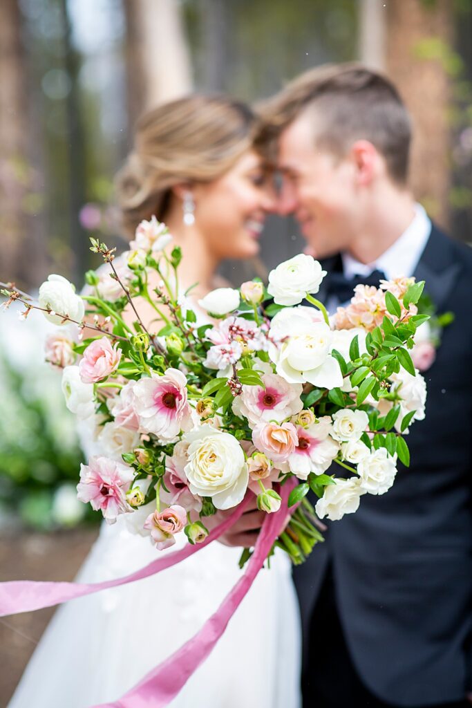 Pink and white bouquet with wedding bride and groom in the background.